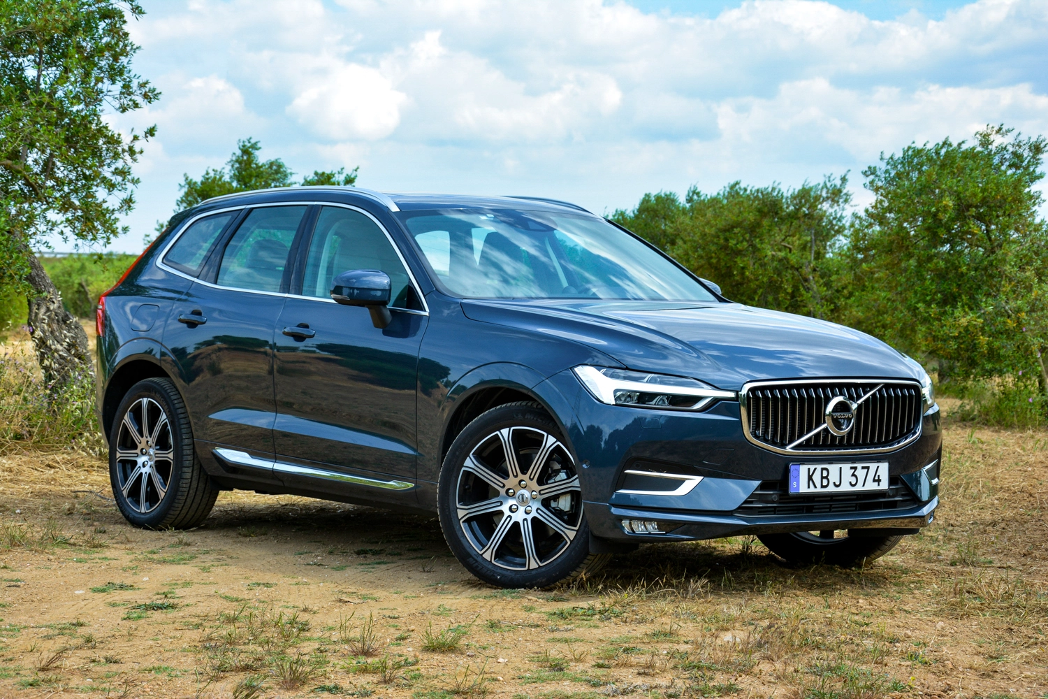 A blue Volvo XC60 parked in a field with bushes around it.