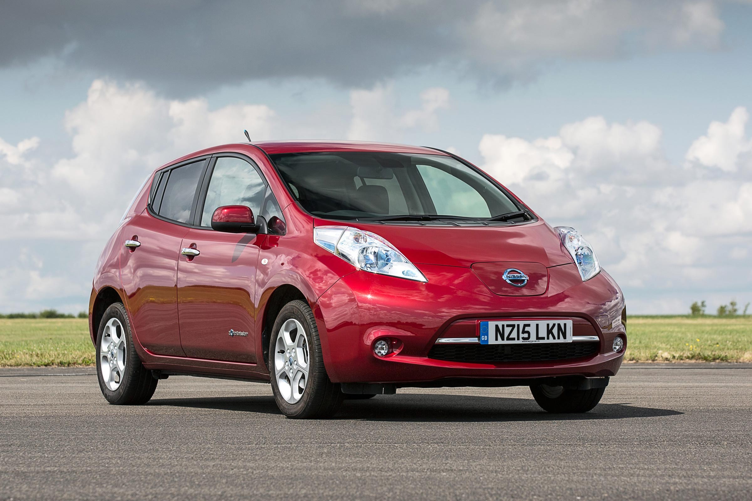 A red Nissan Leaf on an open road, with grass in the background.