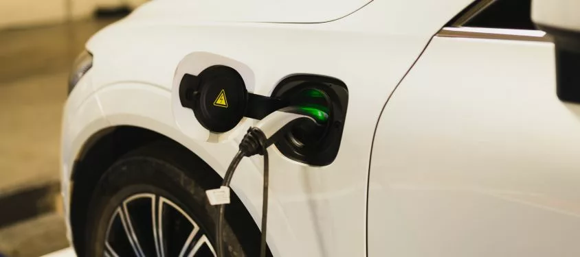 An image of a white electric car charging, with the charger port on the front left of the car.