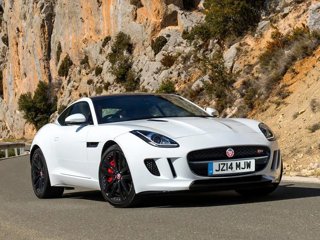 A white Jaguar F-Type on a road with cliffs to the side and sun shining down on it.