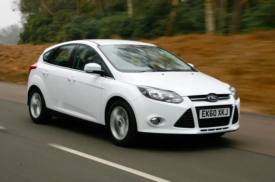 A white Ford Focus driving on a road, with greenery and trees in the background.