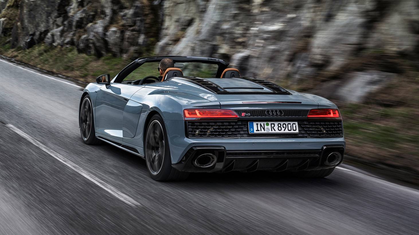 The Audi R8 V10 Spyder Performance Edition in blue/grey with black accents, on an open road.