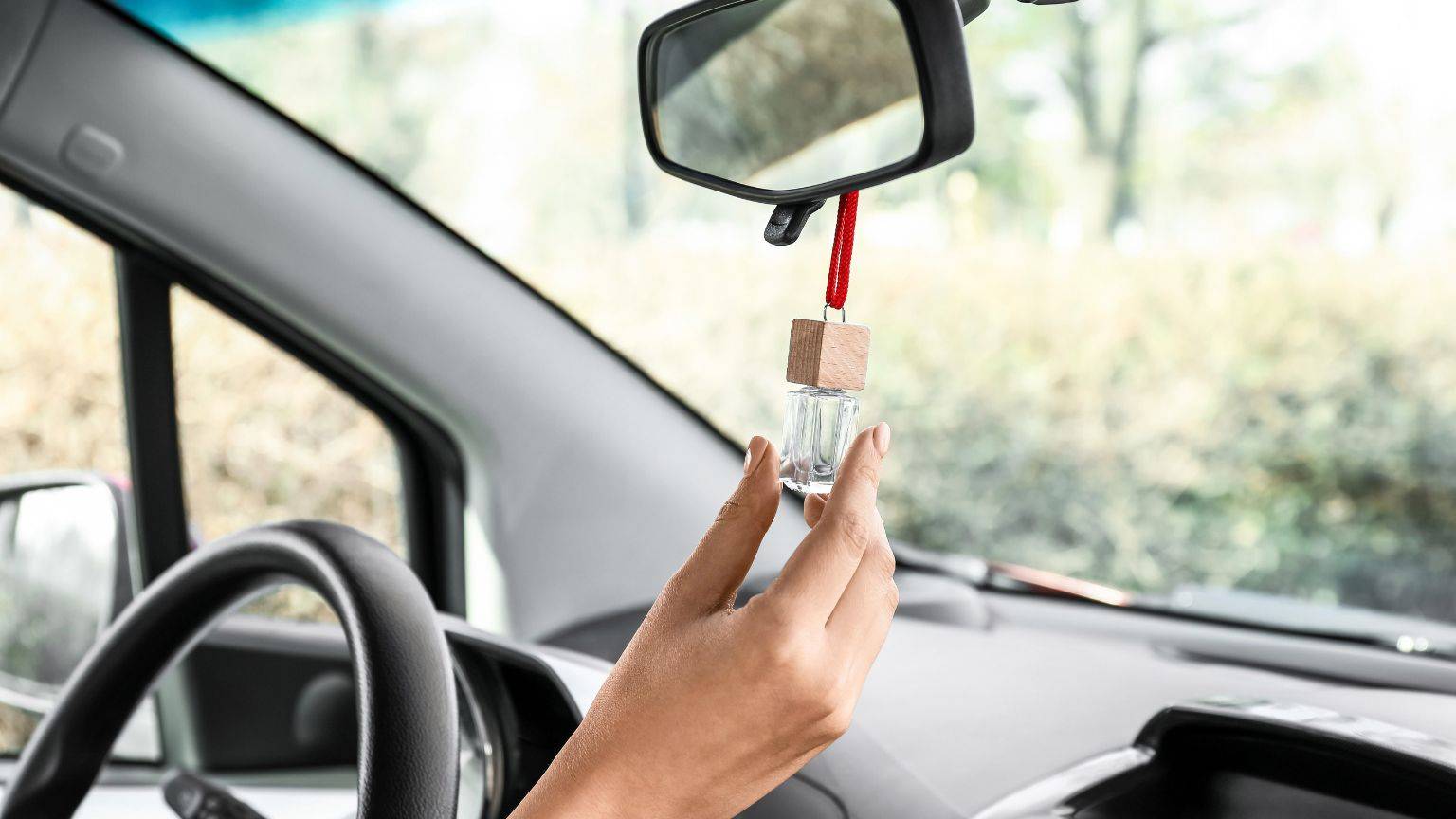 An image of a car interior with a person holding a car air freshener