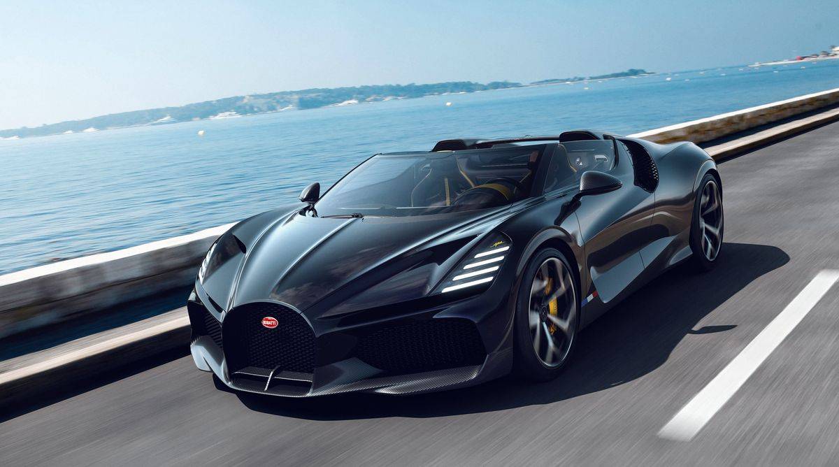 The Bugatti Mistral in black driving on a coastal road with the sea in the background on a sunny day.