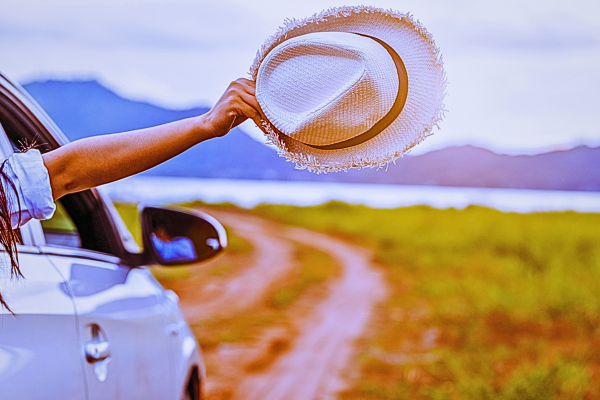 A hand holds a hat out of the window whilst driving on a rural road.