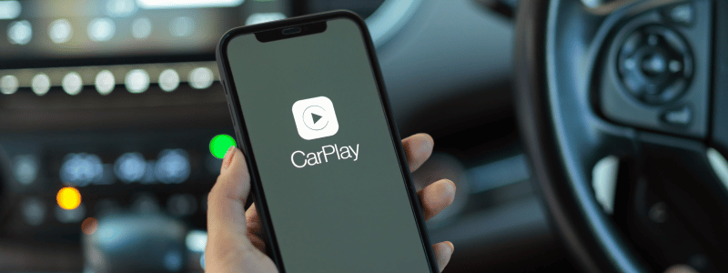 A person operating a phone in a car, with the Apple CarPlay app visible.