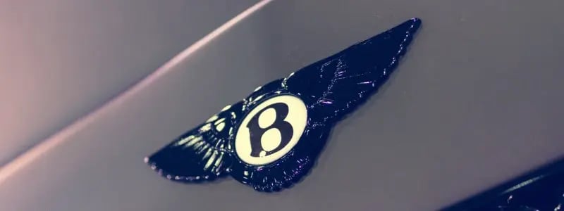 A close up of a Bentley badge on a grey car.