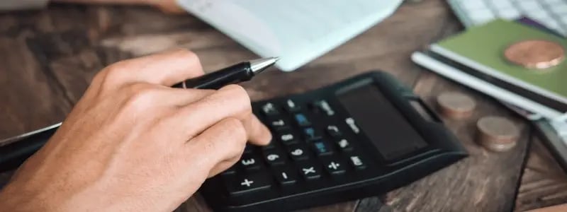 A person using a calculator with coins and credit cards in the background, indicating financial work.