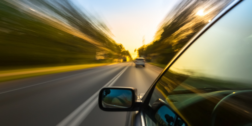 A view down the side of a car driving on a road with a blur effect, indicating the car driving at speed. 