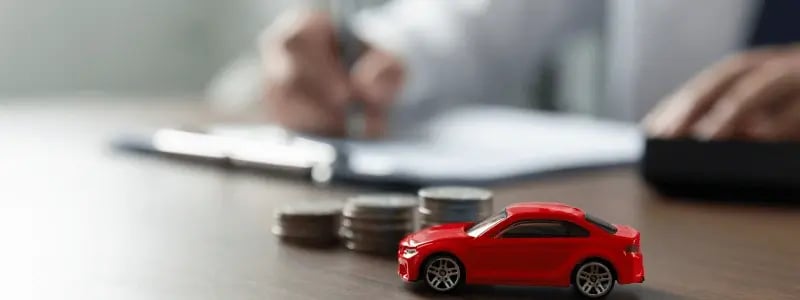 A toy car and stack of coins, with a business professional signing a contract in the background, representing car contract signing.