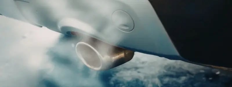 A close up of a car exhaust, with smoke coming out of it.