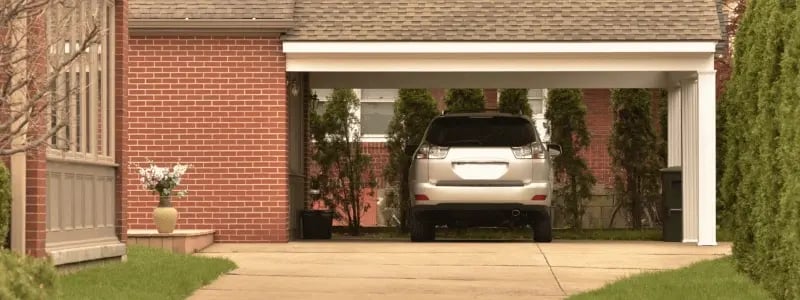 A grey SUV parked under a roof next to a house, with a driveway in the foreground.