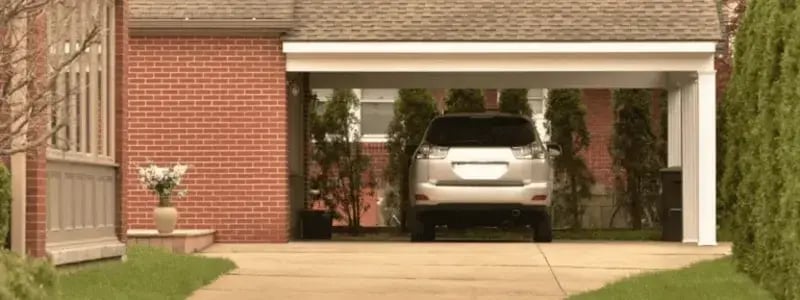 A grey SUV parked under a roof next to a house, with a driveway in the foreground.