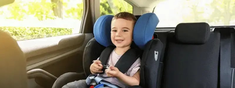 A child smiling whilst sat secured in a car seat.