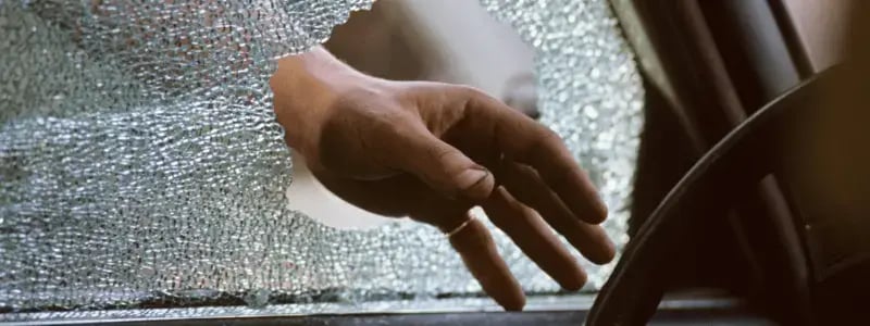 A smashed window with a person's hand reaching through, symbolising car theft.