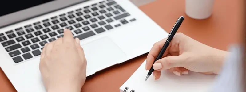 A person writing on a pad and using a laptop.