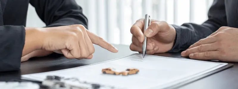 Two people looking at a contract with one ready to sign, and two toy cars on the contract, representing a car related contract.