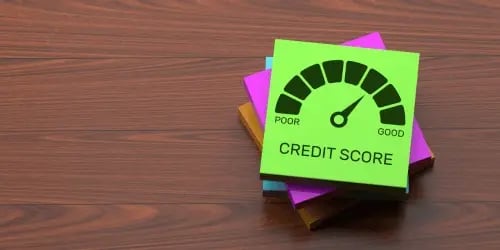 A wooden table with a pile of different coloured post it notes. The top one has a credit score printed on.