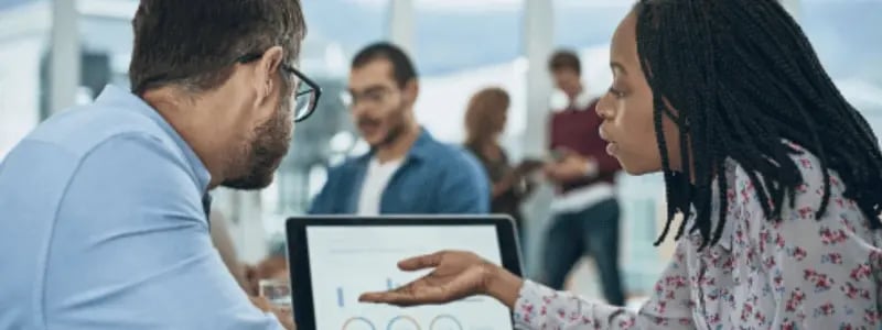 Two people in an office format talk about data findings on a tablet device.