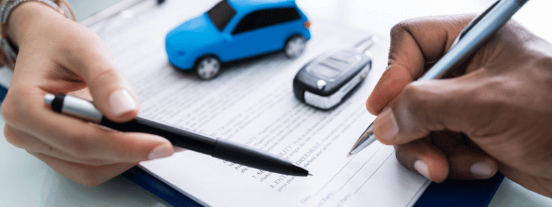 Two hands holding pens above a car contract, with a toy car and car keys on top.
