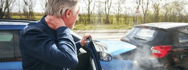 A person looks at the car in front of them stressed, as their car has collided with it.