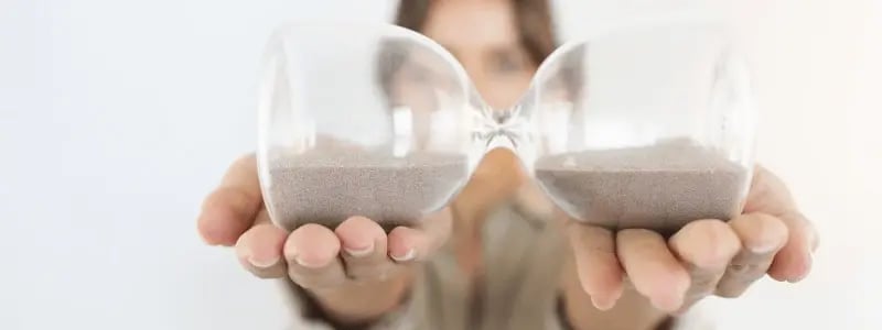 A woman holding an hourglass side on, with equal amounts of sand in each.