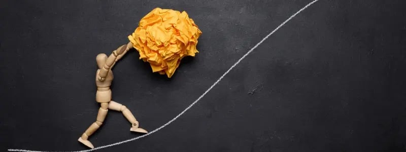 A toy figure pushing a scrunch of paper up a theoretical hill created by an upward line on a chalkboard.