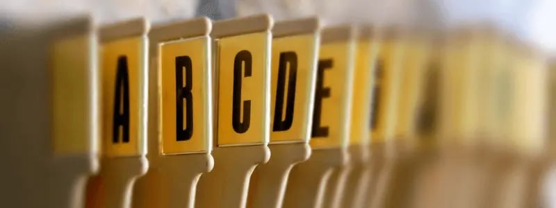 Close-up of yellow file folder tabs labelled alphabetically with bold black letters A to I, arranged in a filing cabinet for organizing documents by name or category.