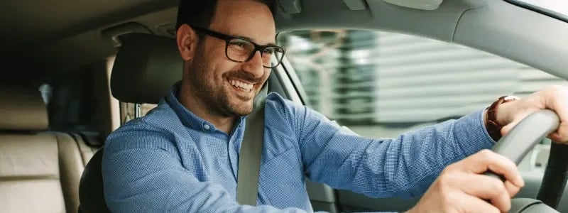 A close up of a person smiling whilst driving their car.