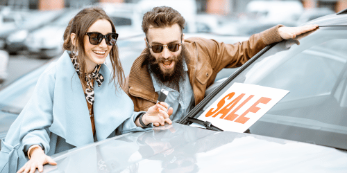 A couple smiling and celebrating a new car.