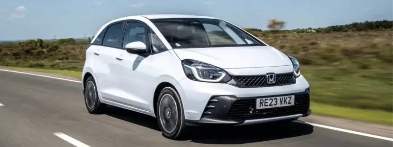 A white Honda Jazz driving on a country road.