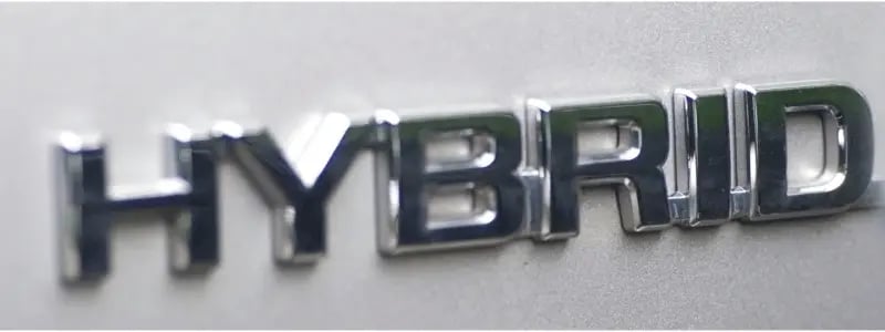 A metal sign close up on a car, reading 'HYBRID', indicating the car is a hybrid.