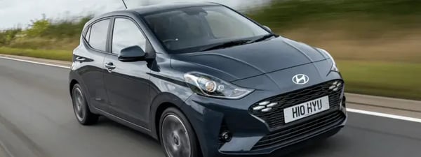 A dark grey Hyundai i10 driving fast on a country road.