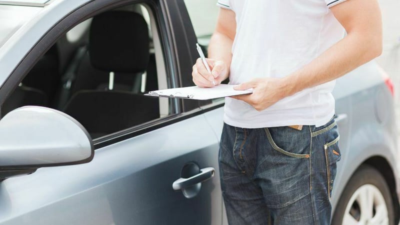 A person writing on a clipboard whilst stood next to a car.