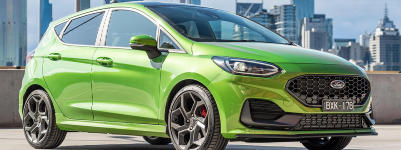 Bright green modern hatchback car parked with a city skyline in the background.