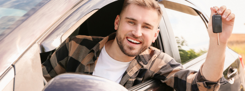 A person holds car keys out of the window whilst smiling.