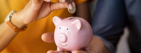 A hand placing a coin into a piggy bank.