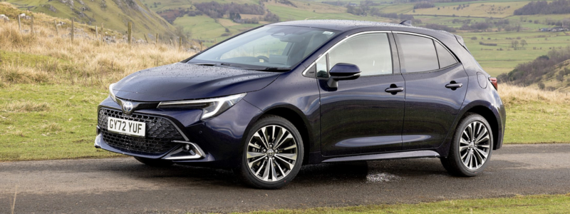 Dark blue Toyota Corolla parked on a roadside with a hilly countryside landscape in the background.