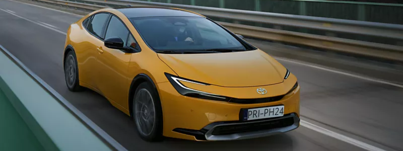 Modern yellow Toyota Prius electric car driving on a motorway with guardrails.