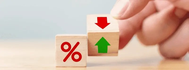 A person moving dices with green and red arrows and percentage signs on, representing rising and falling interest rates.