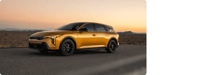 The Kia K4 Hatchback driving on a road in a desert setting at sunset.