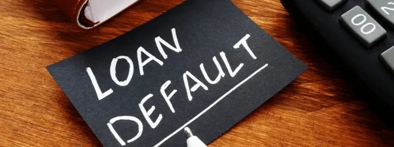 A black card with 'LOAN DEFAULT' written on it, at a desk with a calculator and book next to it.
