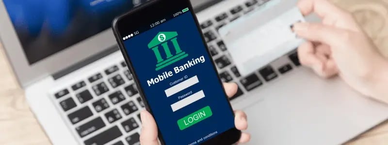 An overhead shot of a login screen for a mobile banking app, with a PC in the background and someone holding up a credit card.