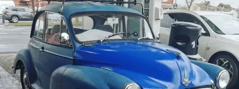 A blue Morris Miner, parked in a petrol station.