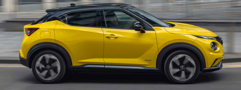 A yellow Nissan Juke driving, with the photo taken from the side. The background is blurred, indicating that the car is moving whilst the photo is being taken.