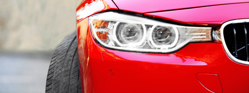 A close up of the front side of a red car, with the headlights showing.