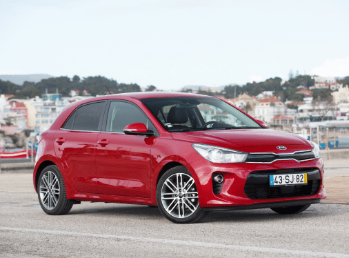 A red Kia Rio parked in a seaside setting.