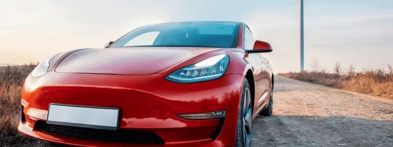 A red Tesla parked in a rural setting, with the number plate empty.