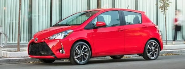 A red Toyota Yaris parked in a city setting.