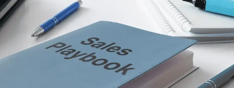 A pen and highlighter sit on a desk and notepads, with a sales playbook in view.